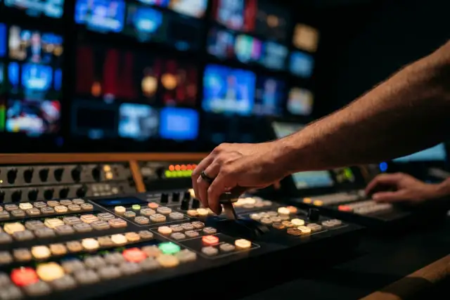 Sala de control de televisión de noche: una mano sobre el mezclador de video, monitores al fondo